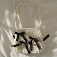 a white crocheted bag with black bows on it